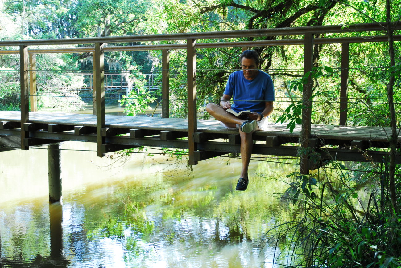 man-reading-bridge-river-green-scenery-plants-relax-laphina-spa-brazil